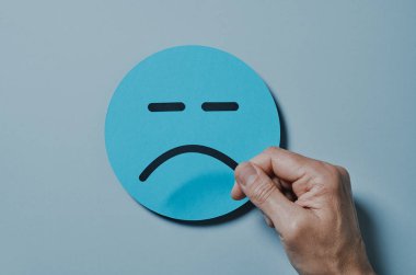 Gri arka planda mavi kağıt bir yüze üzgün bir ağız takan bir adamın yüksek açılı görüntüsü