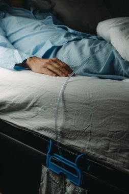 Mavi pijamalı bir adam idrar kateterizasyonu takıyor. Yatakta yüzükoyun yatan bir drenaj torbasına bağlı.