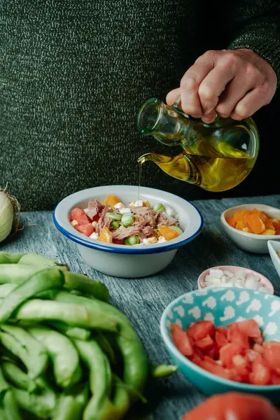 オリーブオイルでドレッシングする男性のクローズアップ 典型的なアンドラルシアの広い豆とサラダ トマト 玉ねぎ 煮た卵 マグロ オレンジ 素朴な灰色の木製のテーブルで — ストック写真