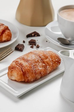 closeup of a xuixo de crema, a pastry filled with custard typical of catalonia, spain, on a white ceramic plate, next to a cup of coffee on a set table clipart