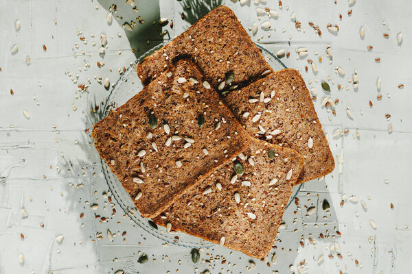 высокий угол обзора стеклянной пластины с кусками ржаного хлеба с семенами льна, на серой текстурированной поверхности