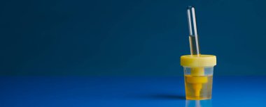 closeup of a sterile container with a sample of urine on a blue surface, in a panoramic format to use as web banner or header clipart