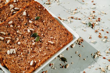 Beyaz dikdörtgen seramik tabakta, gri desenli bir yüzey üzerinde keten tohumlu çavdar ekmeği dilimlerine yakından bakın.