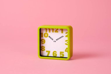 Bir yeşil kare saat, okula geri metin yerine bir saat ve dakika elleri yazılı, pembe bir arkaplan etrafında boş bir alan