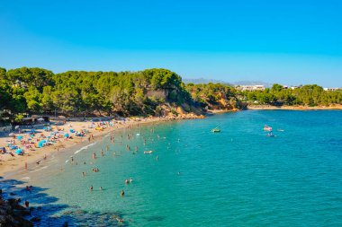 La Ampolla, İspanya - 23 Temmuz 2024: Tatilcilerin güneşli bir yaz gününün keyfini çıkardıkları popüler Costa Daurada kıyısındaki La Ampolla, İspanya 'daki Cap Roig plajı manzarası