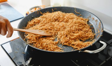 İspanyol Fideua 'sını ev yapımı bir mutfağın fırınında hazırlamak için erişte kızartan bir adamın yakın çekimi.