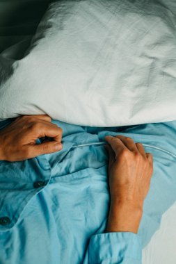 high angle view of a man, in a blue pajamas, handling his urinary catheterization lying in bed clipart