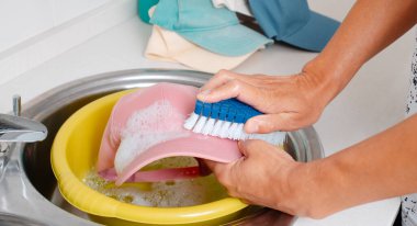 Kafkasyalı bir adam evdeki lavaboda fırça kullanarak şapkasını yıkıyor.