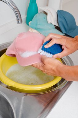 Kafkasyalı bir adamın evdeki çamaşır lavabosunda fırçayla pembe bir şapkayı yıkarken yakın çekimi.