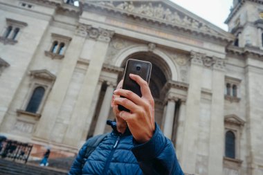 Bir adam Budapeşte, Macaristan 'da Aziz Stephens Bazilikası önünde akıllı telefonuyla selfie çekerken poz veriyor.
