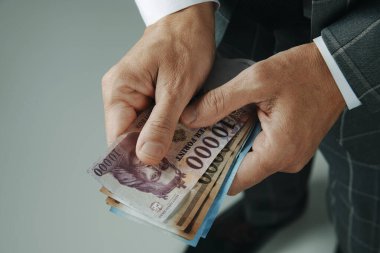 Bir iş adamına yakın çekim, zarif gri bir takım elbise içinde, bazı Macar forint notları içeride duruyor.