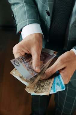 Zarif gri takım elbiseli bir işadamı, içeride ahşap bir zeminde duran bazı Macar forint notlarını sayıyor.