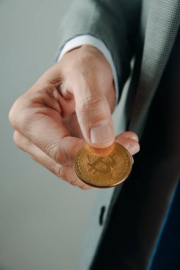 Zarif gri bir takım elbise giyen bir iş adamının kapalı mekanda elinde bir bitcoin tutan bir fotoğrafı.