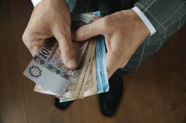 Zarif gri takım elbiseli bir işadamı, içeride ahşap bir zeminde dururken, Macar forint notları sayıyor.