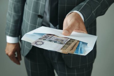 closeup of a businessman, wearing a gray suit, offering an envelope with some hungarian forint notes to the observer indoors clipart