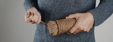 Bir adam bir halat bobininin gevşek ucunu, gri arkaplan üzerinde, web pankartı veya başlık olarak kullanmak için panoramik formatta çeker