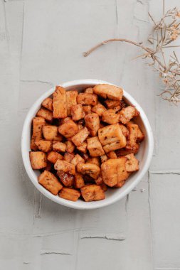 Yüksek açılı beyaz bir kâse ve biraz marine edilmiş tofu küpleri kırsal beton bir yüzey üzerinde atıştırmalık olarak sunuluyor.