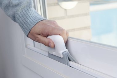 Temizleme cihazı kullanarak beyaz kayan pencere çerçevesini temizleyen bir adamın yakın plan görüntüsü
