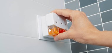 Bir adam elektrikli oda spreyini fayanslı bir banyoda, web pankartı olarak kullanmak üzere panoramik bir formatta prize takar.