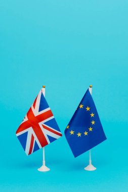 a flag of the United Kingdom and a flag of the European Union standing side by side on a blue background with some blank space on top clipart