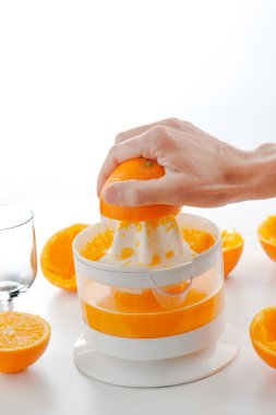 Doğal bir portakal suyu hazırlayan, beyaz bir yüzeye yerleştirilmiş elektrik sıkacağı üzerine portakal sıkan bir adamın yakın çekimi.