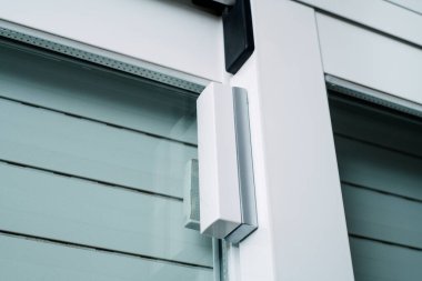 Bir hırsız alarm sisteminin parçası olarak, bir kablosuz cam kırma detektörü ve bir penceredeki bağlantı kırıcının yakın plan görüntüsü