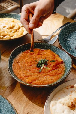 Bir adam açık hava masasında tavuk tika masala servis etmek üzere. Orada bir tabak naan ekmeği ve tavuklu korma var.