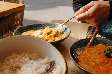 Açık hava masasında tavuk servisi yapan bir adamın yakın plan fotoğrafı. İçinde basmati pilavı olan bir kase ve tavuk tikka masala olan bir tabak.