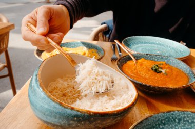 Bir adamın kaseden biraz basmati pilavı alıp, farklı köri ve tavuk ve tikka masala gibi farklı baharatlarla bir açık hava masasında oturması.