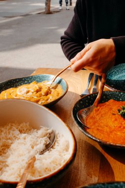 Bir adam açık hava masasında tavuk korması servis etmek üzere. İçinde biraz tavuk tikka masala ve biraz basmati pilavı olan bir tabak var.