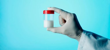 Steril bir konteynırı mavi bir arkaplan önünde, web pankartı olarak kullanmak üzere panoramik bir formatta tutan bir sağlık görevlisi.