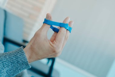 Açık havada bir sandalyede otururken mavi elastik bantla parmaklarını çalıştıran bir adamın bulutları.