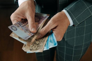 Gri takım elbiseli bir işadamı ahşap bir zeminde duruyor. Odaklanma ve özenle Macar paralarını sayıyor.