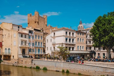 Narbonne, Fransa - 6 Mayıs 2025: Narbonne, Fransa 'daki Kanal de la Robine manzarası, güneşli bir bahar günü, arka planda Başpiskoposlar Sarayı' nın Donjon Gilles Aycelin kulesi görünür