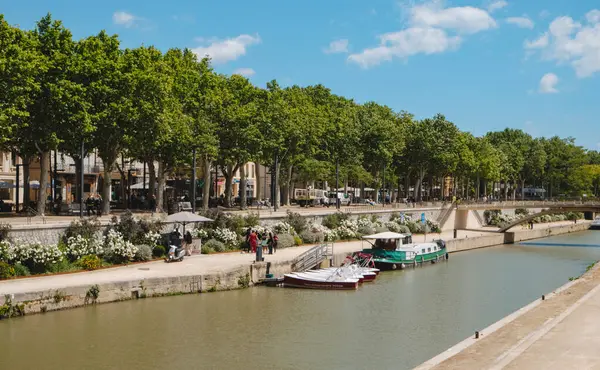 Narbonne, Fransa - 6 Mayıs 2025: Güneşli bir bahar gününde Fransa 'nın Narbonne şehrindeki Rue de la Republique' de ağaçlık gezinti alanı boyunca Kanal de la Robine manzarası