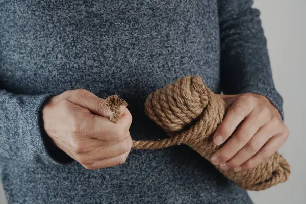 Tarafsız gri bir arkaplan üzerine kurulmuş, birbirine dolanmış bir bobinin gevşek ucunu çeken sıradan giyinmiş bir adamın yakın çekimi.