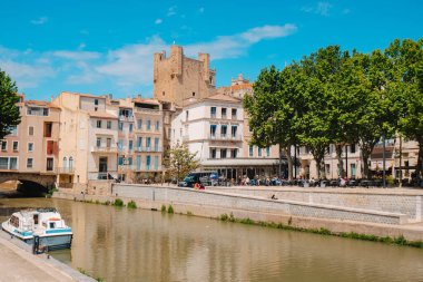 Narbonne, Fransa - 6 Mayıs 2025: Güneşli bir bahar gününde arka planda Donjon Gilles Aycelin kulesi ile Fransa 'nın Narbonne kentindeki Kanal de la Robine' ın manzarası