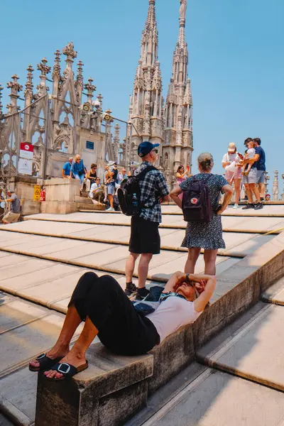 Milan, İtalya - 21 Haziran 2025: Turistler Milano Katedrali 'nin çatısını keşfederken, bir kadın gotik kuleler ve taş mimarinin ortasında sert yaz güneşinden kaçarak gölgede yatıyor