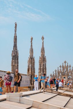 Milan, İtalya - 21 Haziran 2025: Ziyaretçiler Milano Katedrali 'nin çatısını keşfeder, mermer yamaçlar ve kuleler arasında yürürken panoramik manzaranın ve hareketli şehrin üzerindeki yaz güneşinin keyfini çıkarırlar