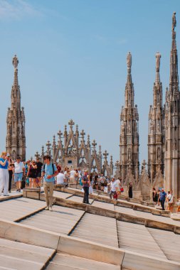 Milan, İtalya - 21 Haziran 2025: Sıcak bir yaz gününde Milano Katedrali 'nin çatısında yürüyen turistler, Gotik kuleler ve gün ortası güneşinin altındaki parlak taşlarla çevrili