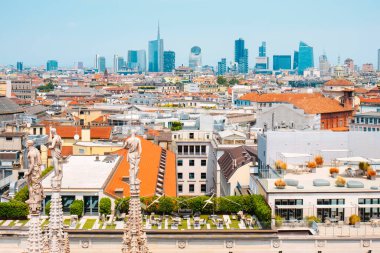 Milan, İtalya - 21 Haziran 2025: Duomo di Milano kulesindeki üç heykel, arka planda Porta Nuova 'nın modern kulelerinin açıkça yükseldiği yoğun bir çatı mozaiğini görmezden geliyor