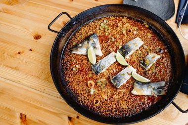 Aynı paella tavasında pilav, kalamar halkaları, dilimlenmiş sebze ve limon dilimleri ile pilav pişirip servis edilen bir deniz levreği.