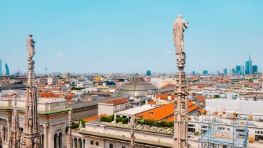 Duomo di Milano 'nun süslü kulesindeki iki mermer heykel çatıların üzerinde duruyor. Milan' ın modern silueti ufka doğru uzanıyor.