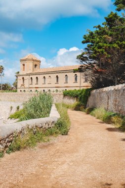 Fransa 'nın Cannes kentindeki Saint-Honorat Adası' ndaki Lerins Manastırı 'na uzanan ve ön planda sazlıklar ve her yer yemyeşil ve yukarıda yumuşak bahar bulutlarıyla çevrili toprak bir yol.