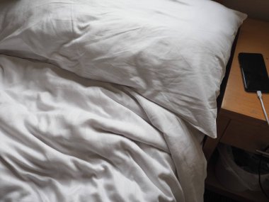 Yatağı yapılmamış, cep telefonu komodinin üzerinde.