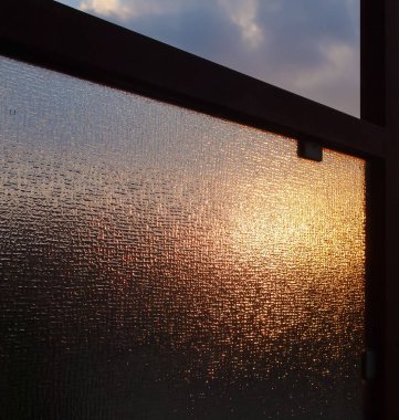 Endüstriyel güneş gün batımında bir camın içinden parlıyor