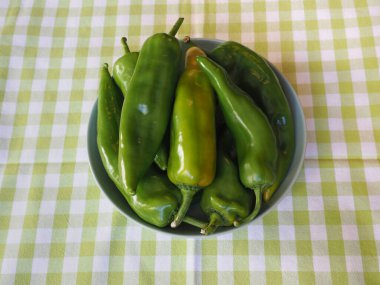 yeşil dolmalık biberler bir tabakta kareli masa örtüsünün üzerinde.