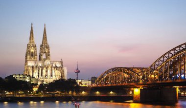 Koelner Dom Sankt Petrus (anlamı: Aziz Peter Katedrali) Gotik kilise ve Hohenzollernbruecke (anlamı: Hohenzollern Köprüsü) Almanya 'nın Koeln kentindeki Rhein nehrinden gece geçer.