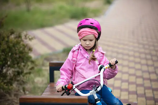 自転車に乗っている少女は動揺している ヘルメットを着てベンチに座っている少女 ストック画像