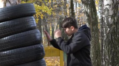 Parkta boks antrenmanı yapan bir çocuk ağaçta asılı duran kum torbasını yumrukluyor..